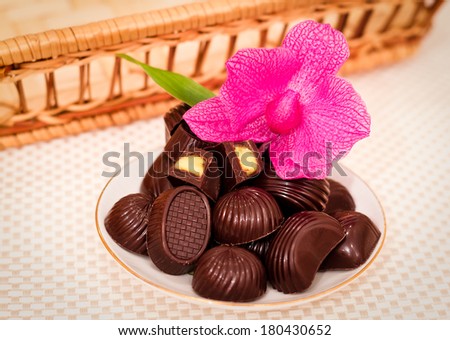 Bunch of delicious sweet chocolates on a saucer with a pink flower on the background of a wicker basket