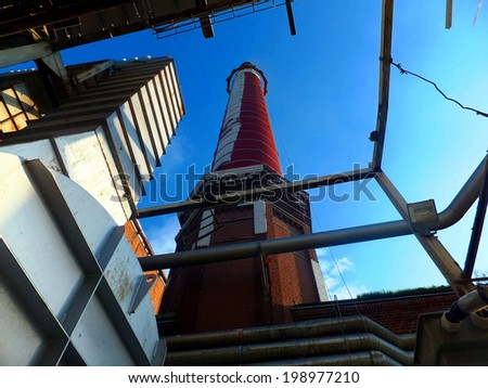 old, tall industrial chimney of brick and exhaust ducts on the background of a cloudless afternoon sky