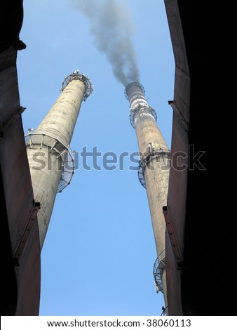 Two chimneys, one fuming in the blue sky and one smoke-free