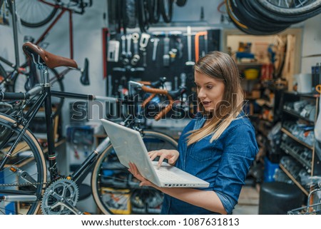 Young female mechanic with laptop. Business woman at a factory. Woman mechanic working on a laptop. Female Bicycle Mechanic.