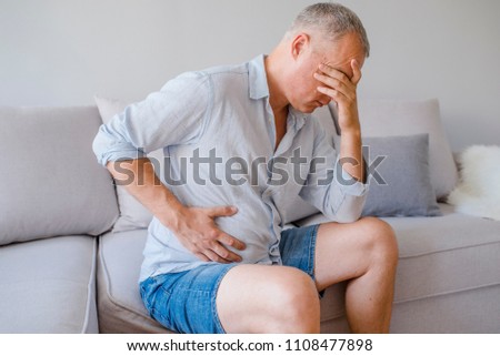 Hand of old man holding stomach suffering from pain, diarrhea, indigestive problem. A middle-aged man has a stomach ache. Unhappy man suffering from stomach ache at home