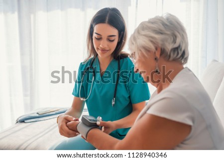 Young nurse measuring blood pressure of elderly woman at home. Female nurse checking blood pressure of a senior woman at home,Home carer checking patients blood pressure