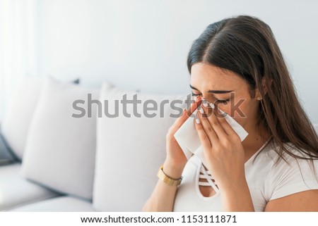 Sick desperate woman has flu. Rhinitis, cold, sickness, allergy concept. Pretty sick woman has runnning nose, rubs nose with handkerchief. Sneezing female.  Brunette sneezing in a tissue