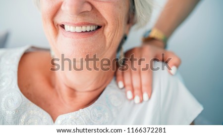 Young elegant woman\'s hand on senior lady\'s shoulder. Portrait of a smiling old lady with her nurse\'s hands on her shoulders. Sign of caring for seniors. Helping hands. Care for the elderly concept.