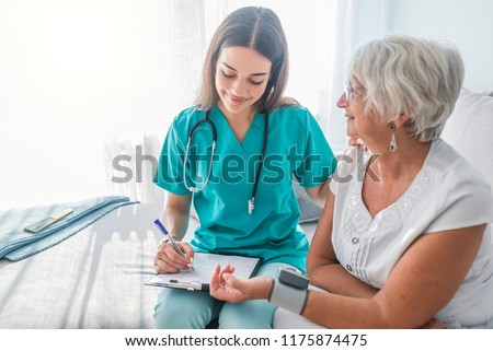 Nurse measuring blood pressure of senior woman at home. Smiling to each other. Young nurse measuring blood pressure of elderly woman at home. Doctor checking elderly woman\'s blood pressure