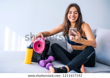Happy fit woman counts calories and made post in blog after fitness workout. Healthy girl wearing sportwear hold smartphone in hand and considers calories in sport app aftrer training.