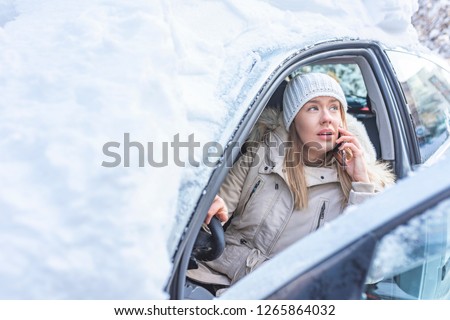 Young woman calling for help or assistance after her car breakdown in the winter. A woman calls for the breakdown services near her snow covered motorcar.