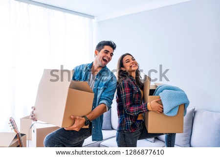 New Home. Funny young couple enjoy and celebrating moving to new home. Happy couple at empty room of new home. Happy couple is having fun with cardboard boxes in new house at moving day.