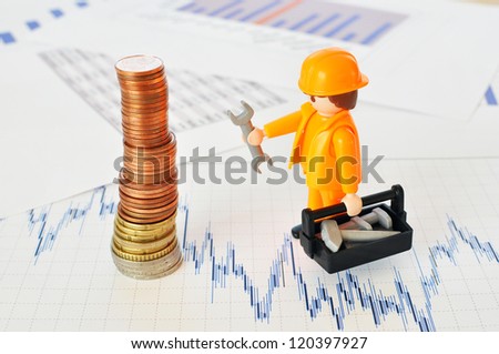 A little worker at a pyramid of coins against financial reports