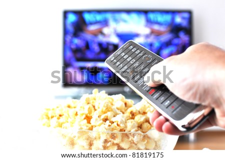 Remote control in the hand against pop-corn and TV-set