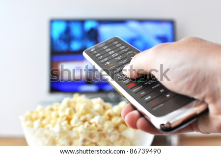 Remote control in the hand against pop-corn and TV-set