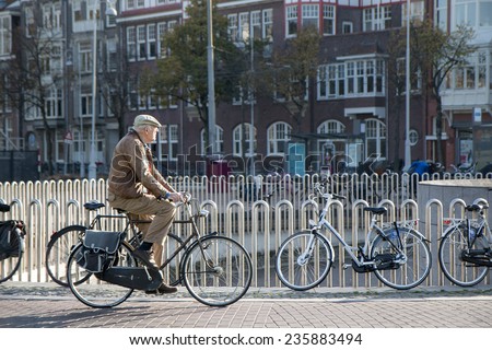 AMSTERDAM, NETHERLANDS - NOV 2014 - An old man making his morning bicycle commute over a canal bridge in the Autumnal Sunshine near Keizersgracht.