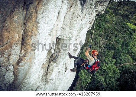 Climber rappelling down cliff with helmet and backpack.