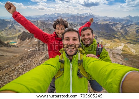 Three friends are a group of hikers having fun and making selfie on the top of the mountain. Happy faces of people who reached success and a amazing peaks landscape