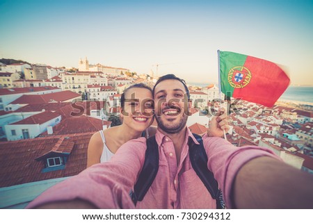 handsome tourists couple take selfie photo with view on Lisbon,Portugal from miradouro on sunny clear day holding portugal flag.Honeymoon loving romantic couple traveling to european city for holiday