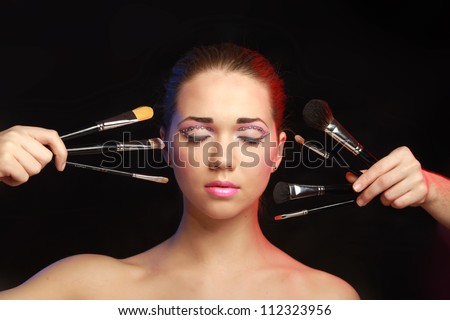 Beautiful young adult woman holds the make-up brushes near attractive face.