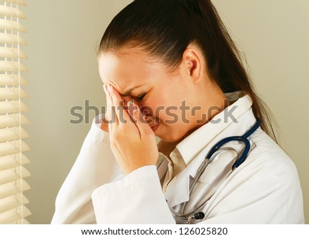 Female doctor with head pain standing near window