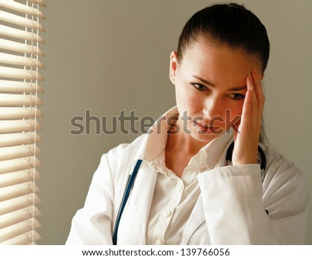 Female doctor with head pain standing near window