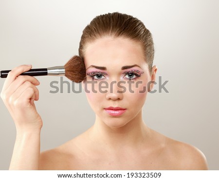 Beautiful young adult woman holds the make-up brushe near attractive face.