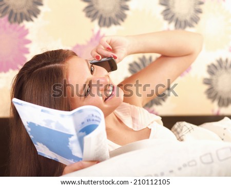 teenager girl lying on a bed reading  book and talking  mobile phone at the same time