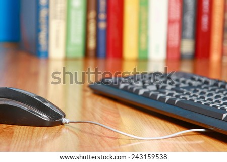 A computer mouse and a keyboard against books on the desk