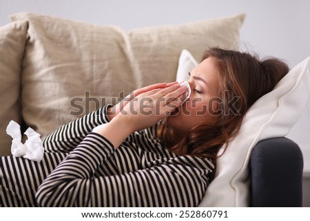 Portrait of a sick woman blowing her nose while sitting on the sofa