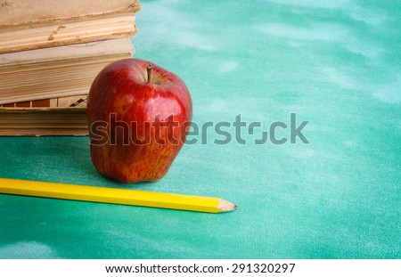 Stack of books with apple and sheet of paper with pencil on it. Isolated on green