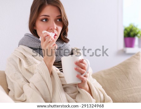 Sick woman covered with blanket holding cup of tea sitting on sofa couch