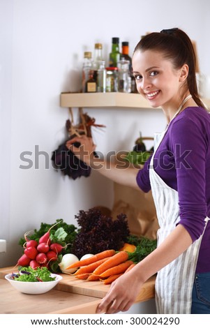Young woman standing in her kitchen near desk with vegetables