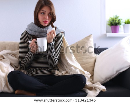 Portrait of a sick woman blowing her nose while sitting on the sofa