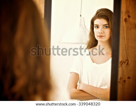 A young woman looking in the mirror .
