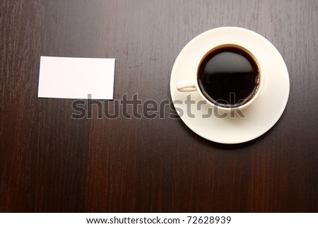 A cup of coffee and a note card from a wooden desk from above