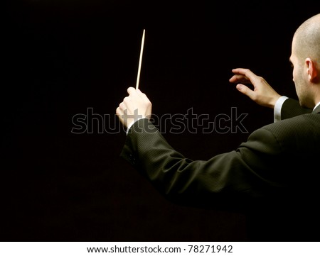 A concert conductor with a baton isolated on a black background, back-view