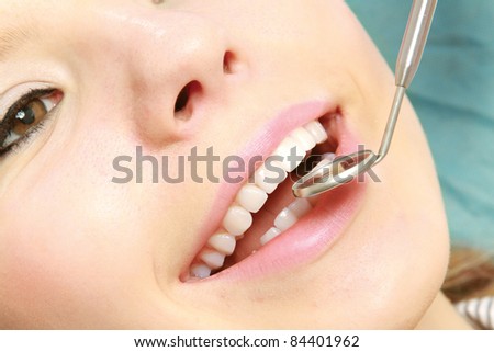 A young woman / teenager with open mouth at the dentist, who uses mirror and a probe for making a diagnosis.
