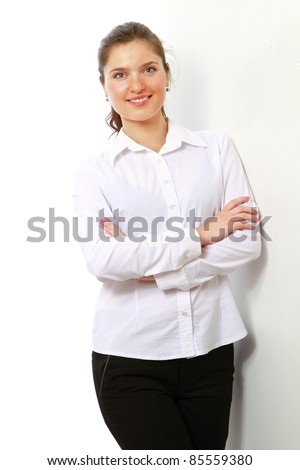 Happy young woman in white shirt standing with folded arms against wall