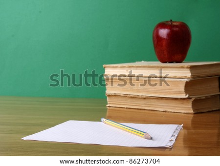 Stack of books with apple and sheet of paper with pencil on it. Isolated on green