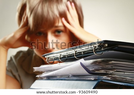 A tired young woman sitting at the desk, having a lot of paperwork to do, focus on a pile of documents