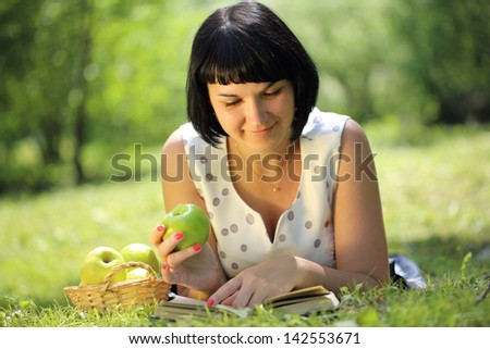 Young woman holding apple and reading book on grass