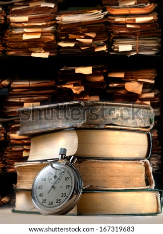 Pile of old books and stopwatch on archive folders background