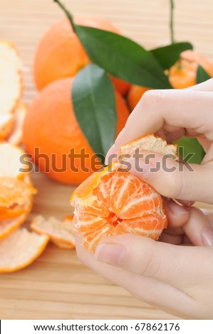 woman hands peeling a ripe tangerine with fresh fruits and leaves on background