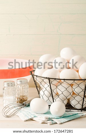 Fresh eggs rest in a wire basket with a vintage bowl and wire whisk, accented with old-fashioned salt and pepper shakers sitting ready for preparing breakfast.