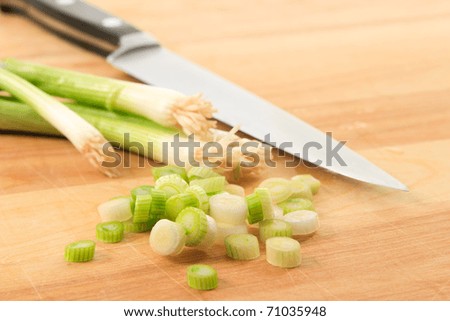 Close up of sliced scallions (green onions) on a wood cutting board with knife