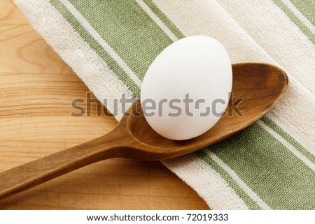 Old wooden spoon holds a whole white egg, set against a green stripped cotton towel includes copy space