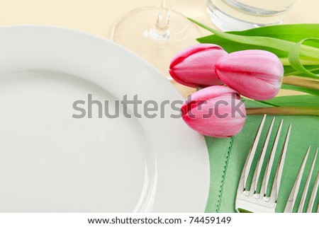 Three pink tulips grace a table setting in fresh Spring colors making a perfect background for Easter or Mother\'s Day promotions - ample copy space provided with the empty white plate
