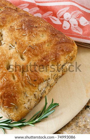 Fresh baked artisan rosemary focaccia bread on a wood cutting board accented with a red towel