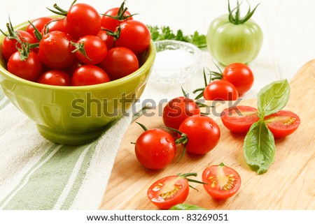 Bowl of ripe red cherry tomatoes with sliced and whole tomatoes on a cutting board accented with basil.
