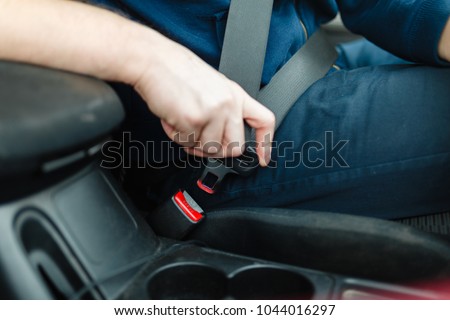 Men\'s hand fastens the seat belt of the car. Close your car seat belt while sitting inside the car before driving and take a safe journey. Closeup shot of male driver fastens seat belt.