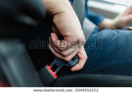 Men\'s hand fastens the seat belt of the car. Close your car seat belt while sitting inside the car before driving and take a safe journey. Closeup shot of male driver fastens seat belt.
