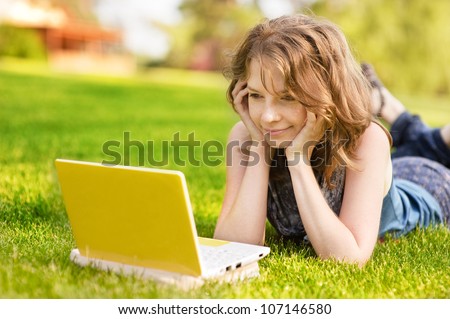 college student lying down on the grass working on laptop at campus