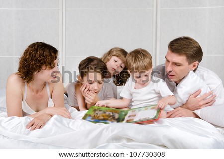 Parents with children are reading book in the bed